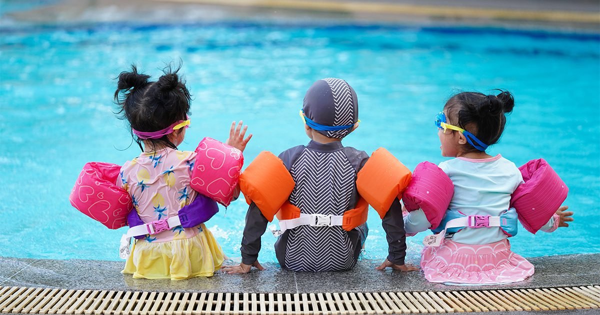 Canadian family practicing water safety at pool with children wearing bright colored swimsuits and life jackets